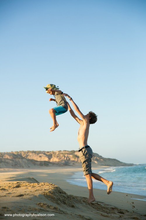 a boy tosses another into the air at a beach