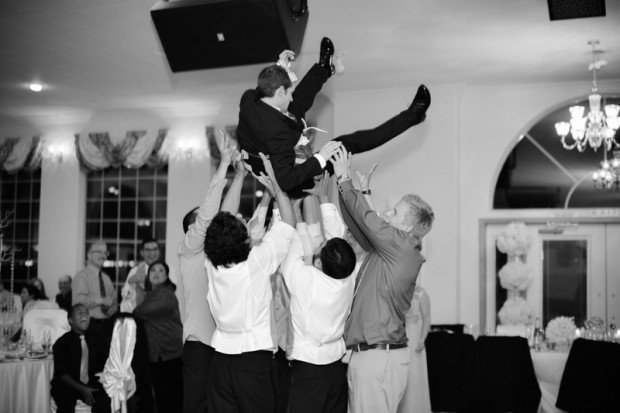 A wedding party tosses the groom in the air